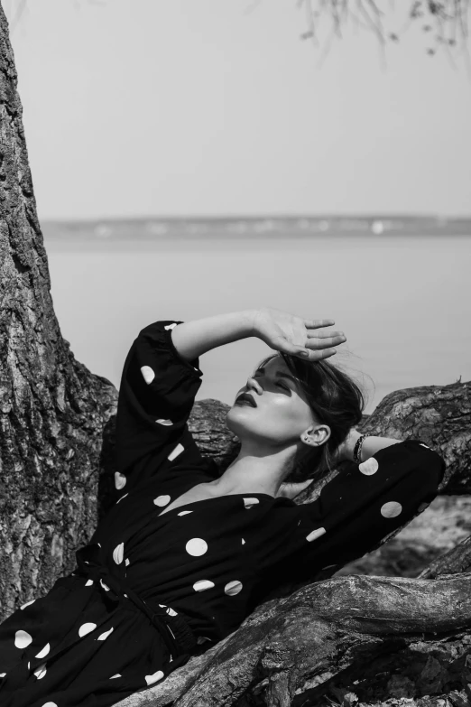 a black and white photo of a woman leaning against a tree, inspired by Grete Stern, unsplash, polka dot, shoreline, laying down, ekaterina