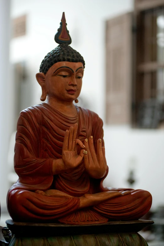 a statue of a buddha sitting on top of a table, seated on wooden chair, hear no evil, religious robes, indoor setting