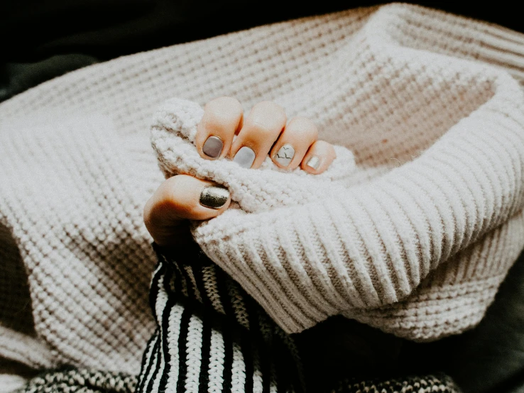 a woman sitting on top of a bed covered in a blanket, trending on pexels, minimalism, nail art, grey sweater, background image, glittering