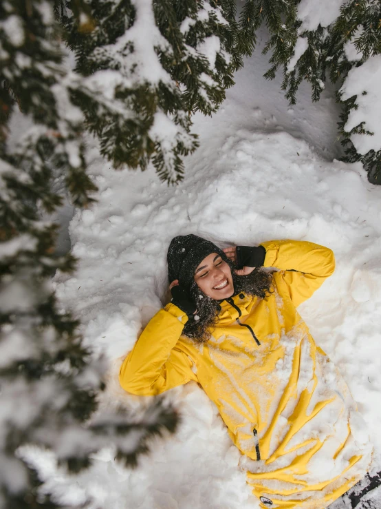 a woman in a yellow jacket laying in the snow, pexels contest winner, smiling down from above, avatar image, adventure, thumbnail