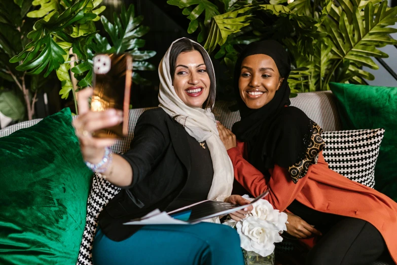 a couple of women sitting on top of a couch, a picture, inspired by Maryam Hashemi, pexels contest winner, hurufiyya, taking a selfie, with ivy, event photography, hijab