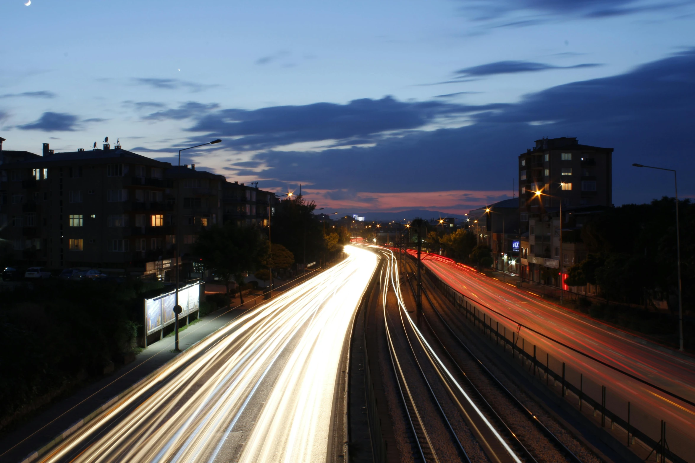 a city street filled with lots of traffic at night, a picture, by Kristian Zahrtmann, unsplash, trains, late summer evening, light streaks in the sky, taken on a 2010s camera