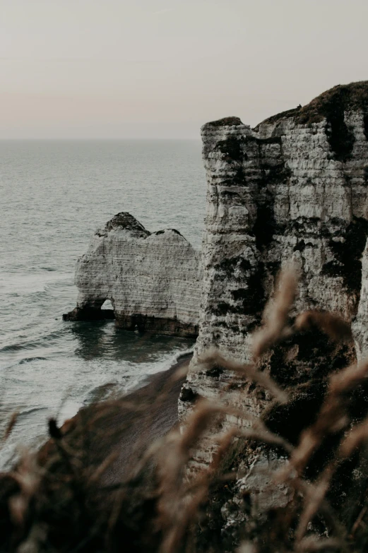 a couple standing on top of a cliff next to the ocean, over a chalk cliff, autumnal, rock arches, unsplash 4k