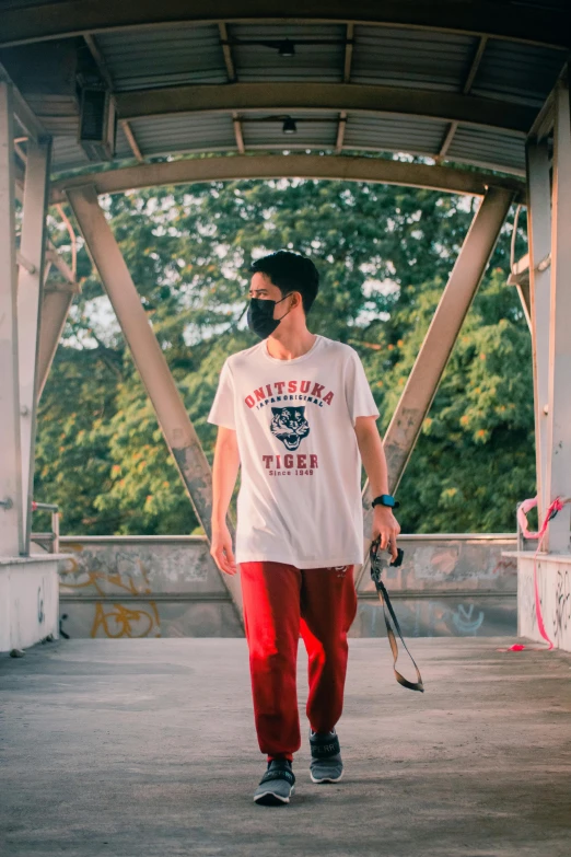 a man in a white shirt holding a skateboard, by Julia Pishtar, pexels contest winner, masked face, standing on a bridge, red shirt brown pants, ( ( theatrical ) )
