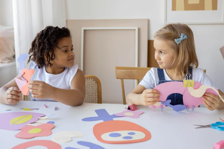 two little girls sitting at a table making crafts, inspired by Karel Appel, pexels contest winner, kirigami, crown made of felt, youtube thumbnail, alternate angle