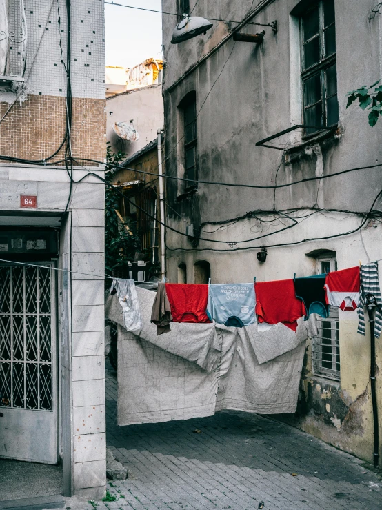 clothes hanging out to dry on a clothes line, an album cover, by Elsa Bleda, unsplash contest winner, in a narrow chinese alley, soft grey and red natural light, tel aviv street, photo of poor condition