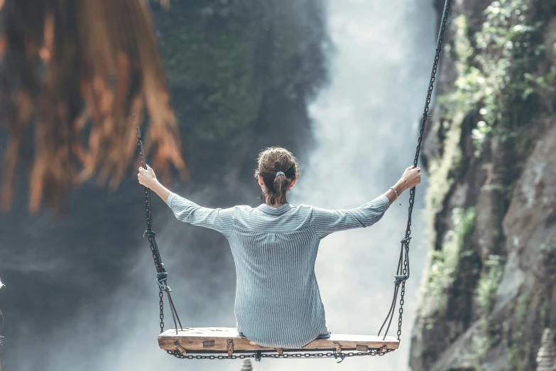 a man sitting on a swing in front of a waterfall, by Matija Jama, pexels contest winner, panoramic view of girl, over the shoulder view, avatar image, relaxed expression