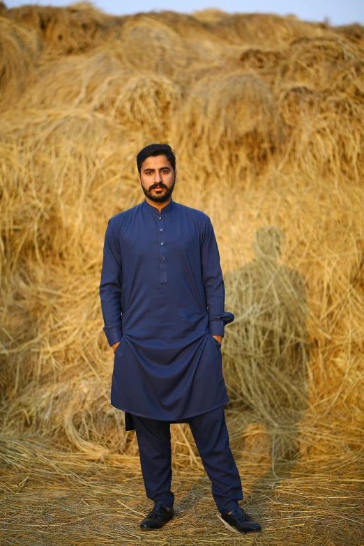 a man standing in front of a pile of hay, an album cover, inspired by Manjit Bawa, pexels contest winner, blue uniform, wearing a kurta, hammershøi, catalog photo