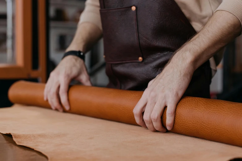 a man that is standing next to a roll of paper, by Tom Bonson, trending on pexels, arts and crafts movement, leather interior, brown, hand made, creating a soft