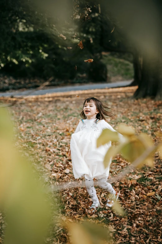 a little girl that is standing in the leaves, inspired by Kate Greenaway, unsplash, smiling and dancing, low quality photo, japanese, white