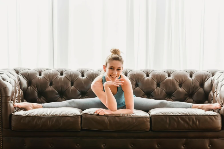 a woman laying on top of a brown couch, arabesque, sydney sweeney, doing splits and stretching, relaxing and smiling at camera, profile image
