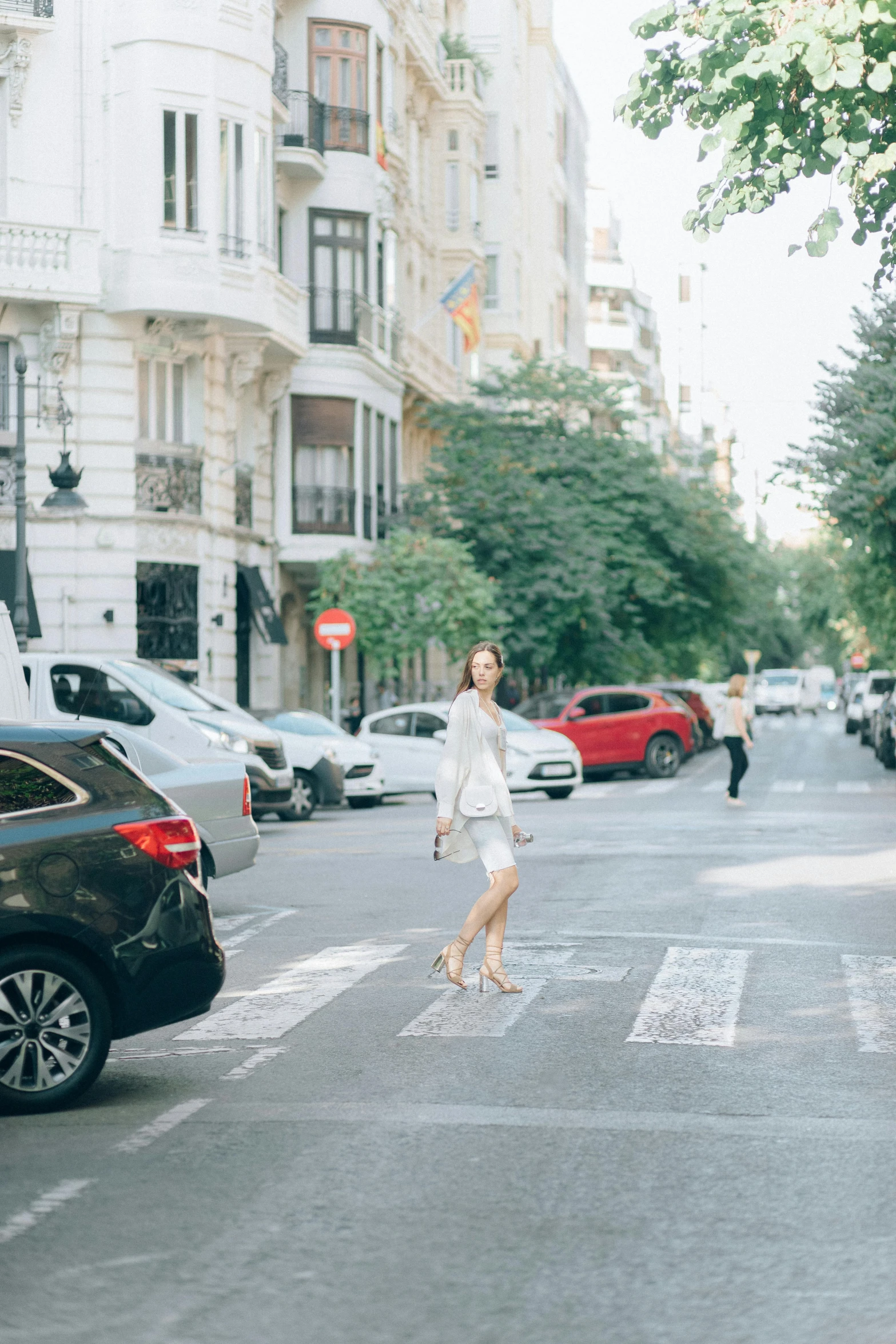 a woman walking across a street next to parked cars, a picture, inspired by Eva Gonzalès, trending on unsplash, wearing white skirt, square, madrid, conde nast traveler photo