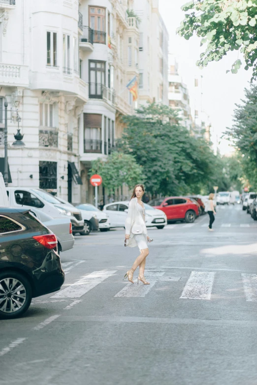 a woman walking across a street next to parked cars, a picture, inspired by Eva Gonzalès, trending on unsplash, wearing white skirt, square, madrid, conde nast traveler photo