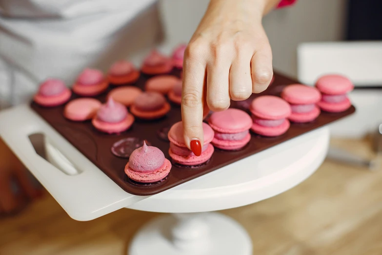 a close up of a person holding a tray of macarons, by Julia Pishtar, trending on pexels, magenta colours, frying nails, instruction, crimson themed