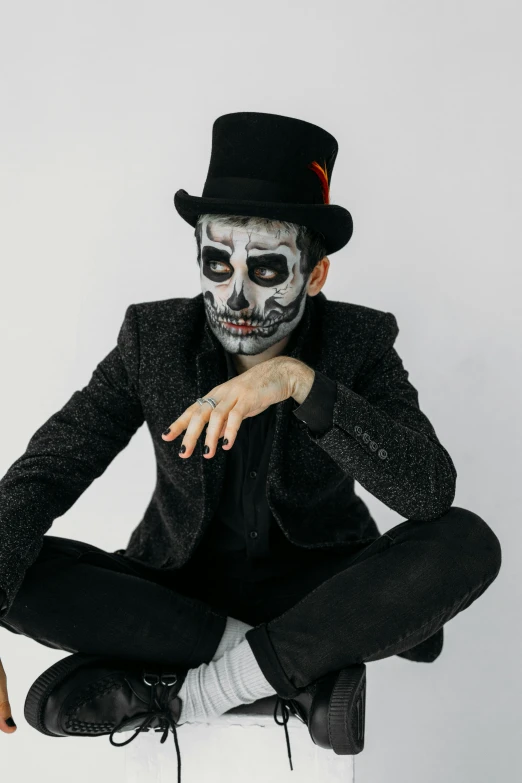 a man dressed as a skeleton sitting on a stool, inspired by James Bolivar Manson, trending on pexels, black top hat, face painting, pete davidson, symmetrical face and body