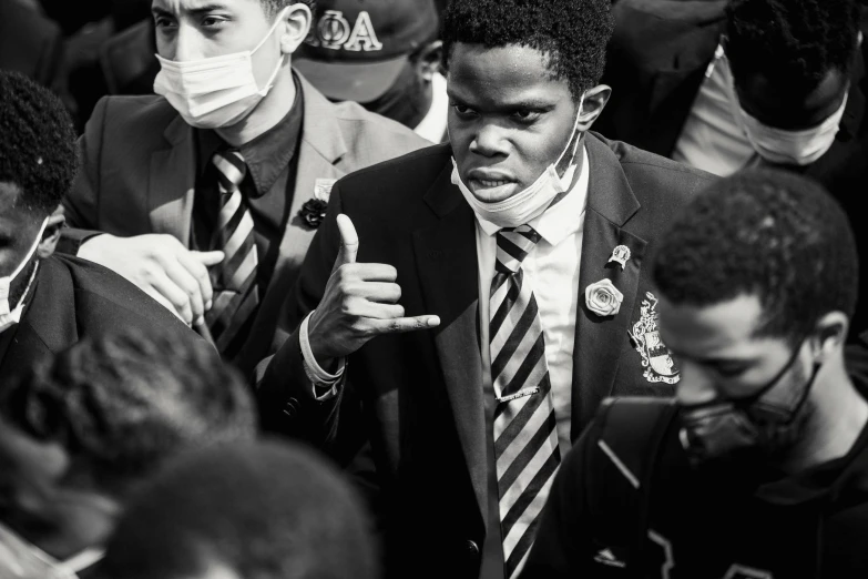 a man in a suit and tie giving a thumbs up, a black and white photo, pexels, renaissance, black teenage boy, protest movement, people are wearing masks, looking confused