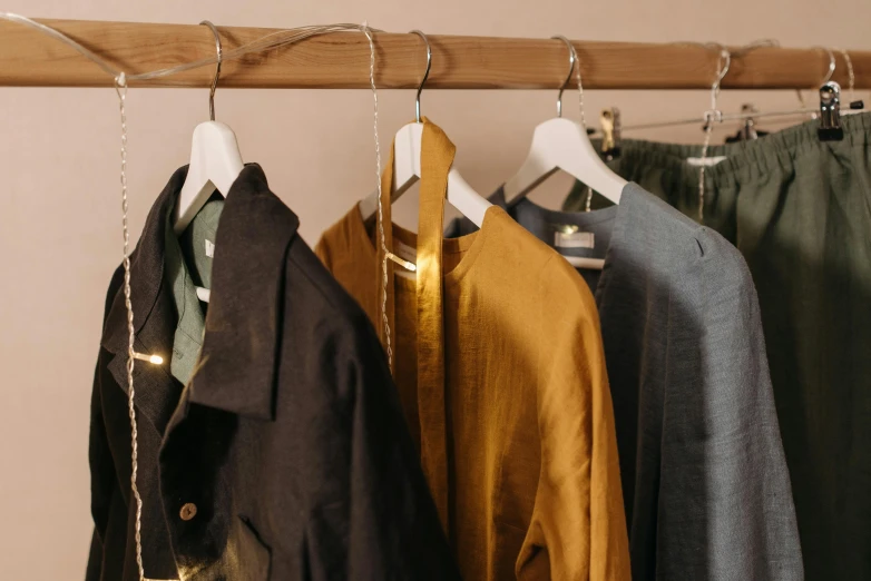 a row of clothes hanging on a clothes rack, by Emma Andijewska, trending on pexels, private press, yellow and charcoal leather, wearing a linen shirt, robes with golden characters, in the style wes anderson