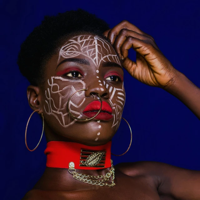 a woman with white paint on her face, an album cover, by Lily Delissa Joseph, pexels contest winner, afrofuturism, blue and red tattoo, gold bodypaint, wearing shipibo tattoos, man is with black skin