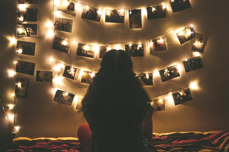 a woman sitting on top of a bed under a string of lights, a polaroid photo, trending on pexels, visual art, pinterest hair picture, symmetric lights, teenager hangout spot, lots of pictures