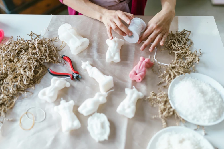 a woman sitting at a table making marshmallows, a marble sculpture, by Jessie Algie, unsplash, sanrio ornaments, upcycled, white candles, hanging beef carcasses