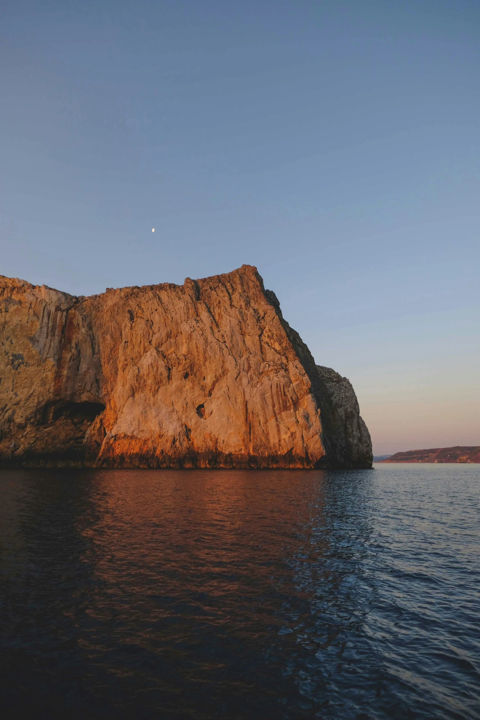 a large rock in the middle of a body of water, by Ryan Pancoast, croatian coastline, slide show, warm glow, half moon