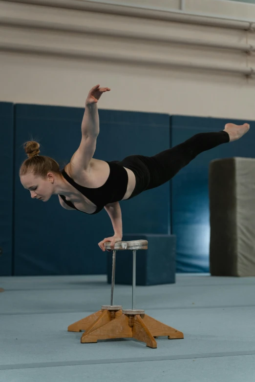 a woman doing a handstand on a stool in a gym, inspired by Elizabeth Polunin, arabesque, birds eye, elliot anderson, julia hetta, competition winning