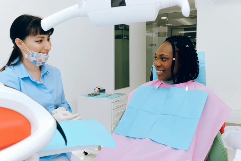 a woman sitting in a chair in a dentist's chair, a colorized photo, pexels contest winner, hurufiyya, dark-skinned, youtube thumbnail, clean medical environment, with a whitish