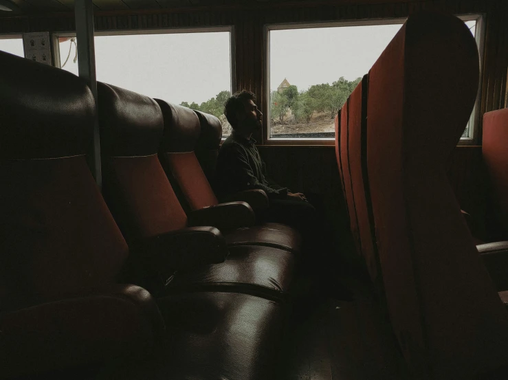 a person sitting in a chair in front of a window, an album cover, by Attila Meszlenyi, pexels contest winner, happening, on a boat, dark skinned, ship interior, inside the train