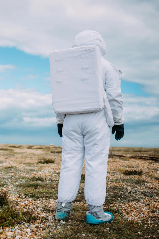 a person in a white suit standing on a field, wearing nanotech honeycomb robe, looking out over the sea, wearing dirty flight suit, with a backpack