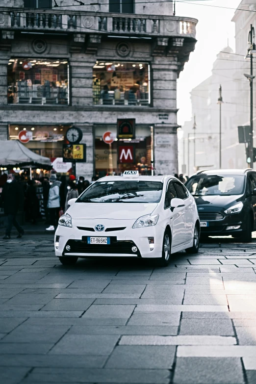 a white car driving down a street next to tall buildings, pexels contest winner, happening, taxis, hydrogen fuel cell vehicle, italian, square