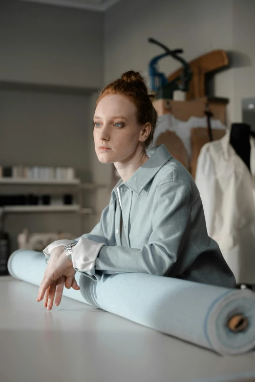 a woman sitting on top of a table next to a roll of paper, trending on pexels, hyperrealism, hr ginger, fabrics, androgynous person, wearing a light blue shirt