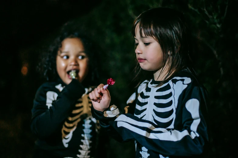 a couple of little girls standing next to each other, pexels contest winner, vanitas, glowing bones, snacks, dark outside, boys