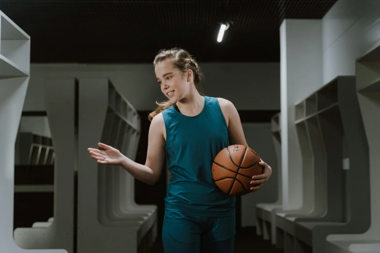 a woman standing in a locker holding a basketball, by Emma Andijewska, pexels contest winner, happening, teal uniform, excited, slight overcast lighting, in the middle of an arena