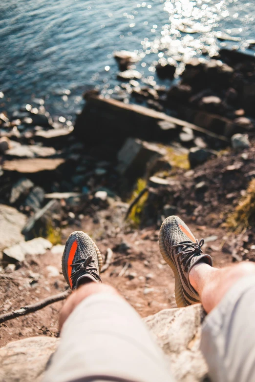 a person sitting on a rock next to a body of water, sneakers, lying down, up close, ben watts
