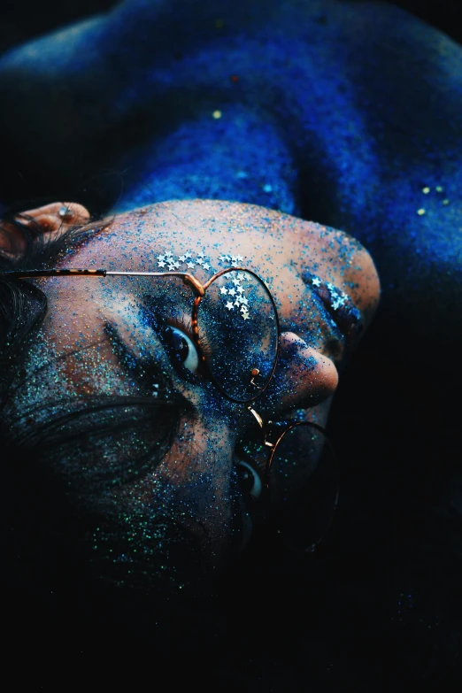 a man laying on top of a bed covered in blue paint, inspired by Elsa Bleda, trending on pexels, glitter gif, dark-skinned, stars in her gazing eyes, beautiful shades