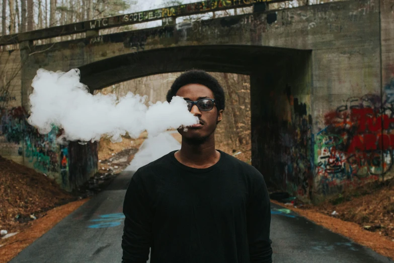 a man standing in the middle of a road with smoke coming out of his mouth, pexels contest winner, graffiti, black teenage boy, holding a small vape, shades, pipe jungle