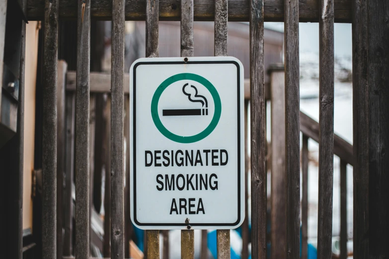a no smoking sign on a wooden fence, by Julia Pishtar, pexels, buildings and smoke, portrait image, recessed, standing near the beach