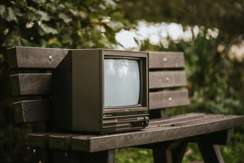 an old television sitting on top of a wooden bench, inspired by Anne Nasmyth, unsplash, cast, outside, brown, a green