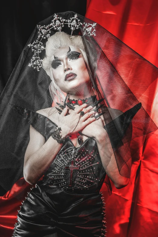 a woman in a black dress with a veil over her head, an album cover, inspired by Hedi Xandt, featured on reddit, international gothic, red and black flags, ru paul\'s drag race, detail shot, monochrome and red color bleed