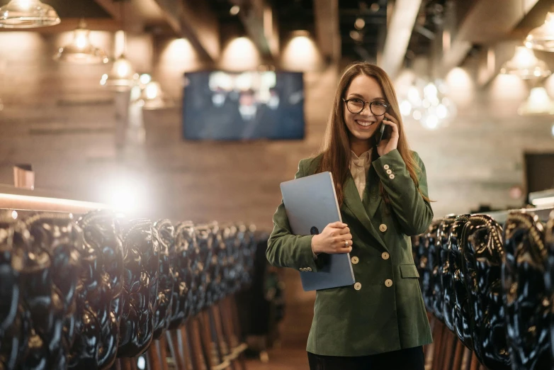 a woman in a green jacket talking on a cell phone, trending on pexels, lecture halls and gambling dens, wearing a suit and glasses, standing in an arena, inside a grand