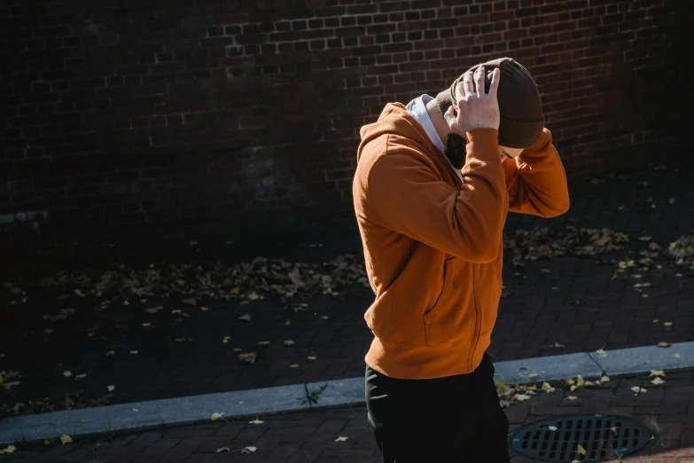 a man walking down a street talking on a cell phone, unsplash, visual art, orange hoodie, facepalm, with his hands in his hair, hiding behind a brick wall