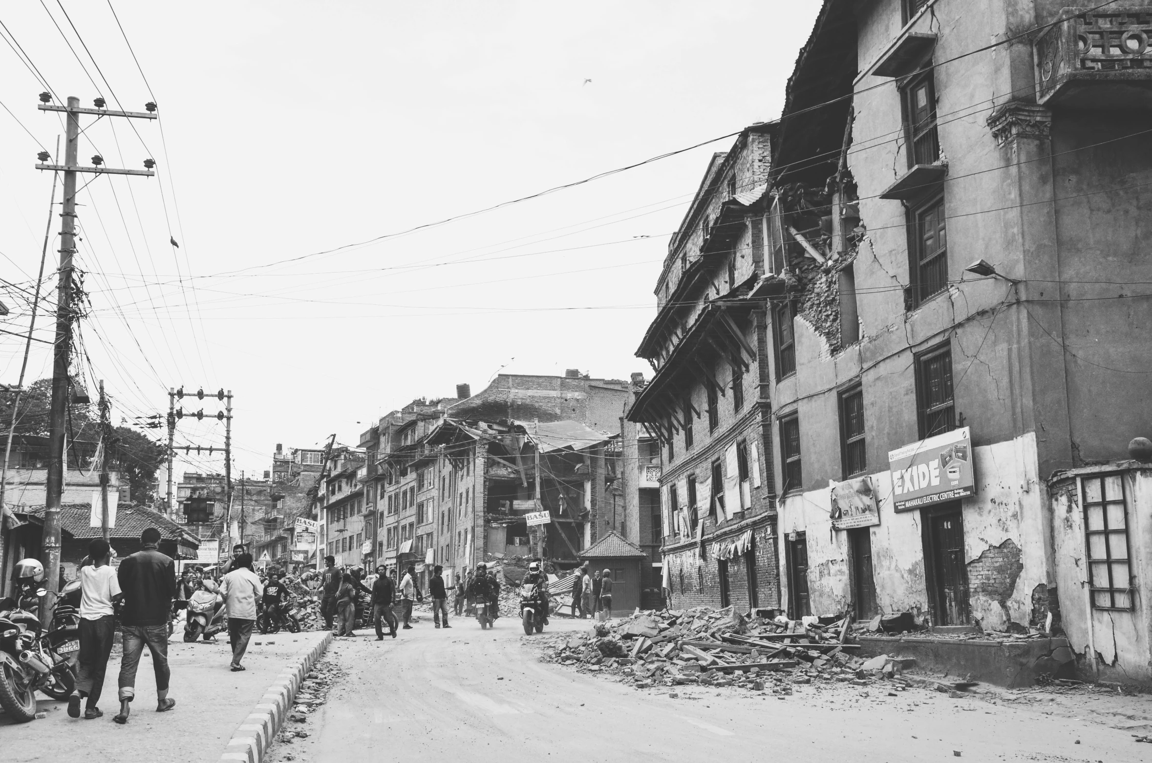 a black and white photo of people walking down a street, wrecked buildings, nepal, in the middle of the city, beige