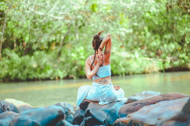 a woman sitting on top of a rock next to a river, by Aya Goda, unsplash, hurufiyya, brunette fairy woman stretching, ( ( ( ( kauai ) ) ) ), cottagecore!! fitness body, slide show