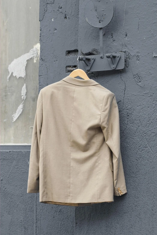 a jacket hanging on the side of a building, wear's beige shirt, 3 / 4 back view, color photograph, gray canvas