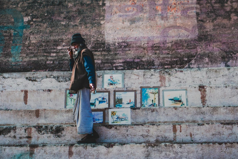 a man standing in front of a wall with pictures on it, a picture, inspired by Steve McCurry, pexels contest winner, street art, steps, hindu aesthetic, vintage color, “ painting