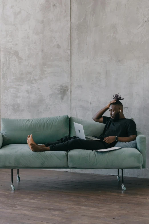 a man sitting on a couch with a laptop, pexels contest winner, minimalism, jaylen brown, curls on top of his head, black furniture, performing