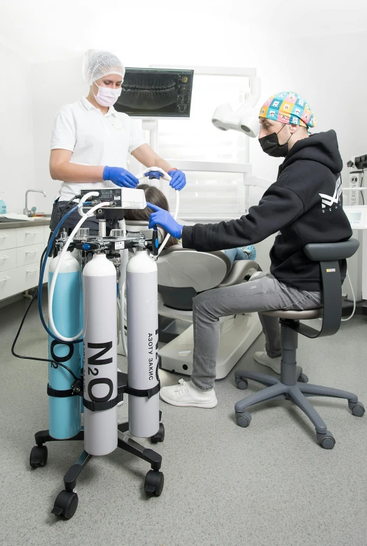 a couple of people that are in a room, sharing an oxygen tank, helmet on, dentist, grey