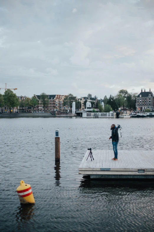 a man standing on a dock next to a body of water, by Jacob Toorenvliet, gigapixel photo, amsterdam, full body 8k, timelapse