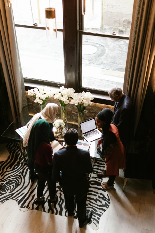 a group of people standing in front of a window, hurufiyya, wide overhead shot, networking, luxurious environment, papers on table