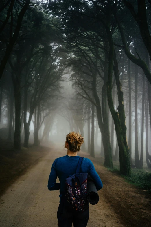 a woman walking down a dirt road on a foggy day, pexels contest winner, renaissance, trekking in a forest, back turned, forest city streets behind her, pictured from the shoulders up